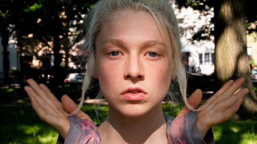 Hunter Schafer posant en extérieur sous une lumière naturelle douce, portant de longs gants sans doigts et regardant calmement la caméra.