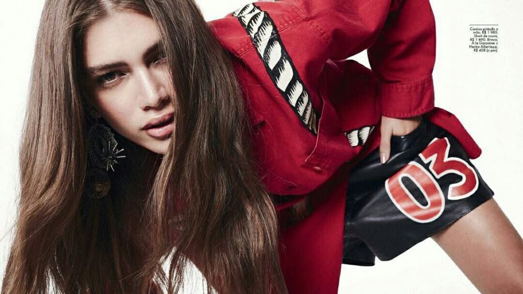 Valentina Sampaio portant un haut rouge et un short noir, penchée en avant lors d’un shooting photo de mode.