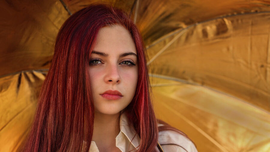 Jeune femme aux longs cheveux rouges se tenant devant un fond doré.