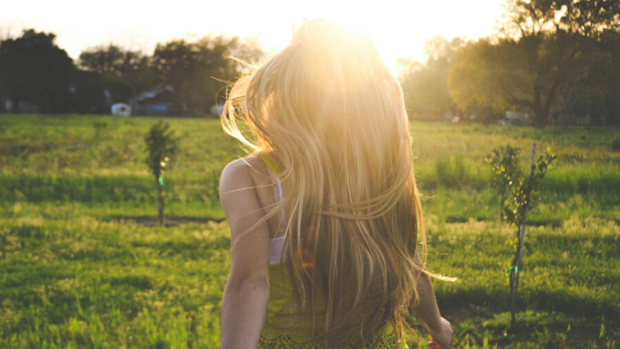 Femme aux longs cheveux blonds marchant à travers un champ au coucher du soleil.