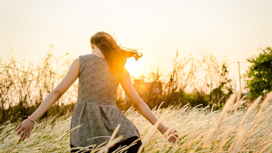Jeune femme marchant à travers un champ au coucher du soleil.