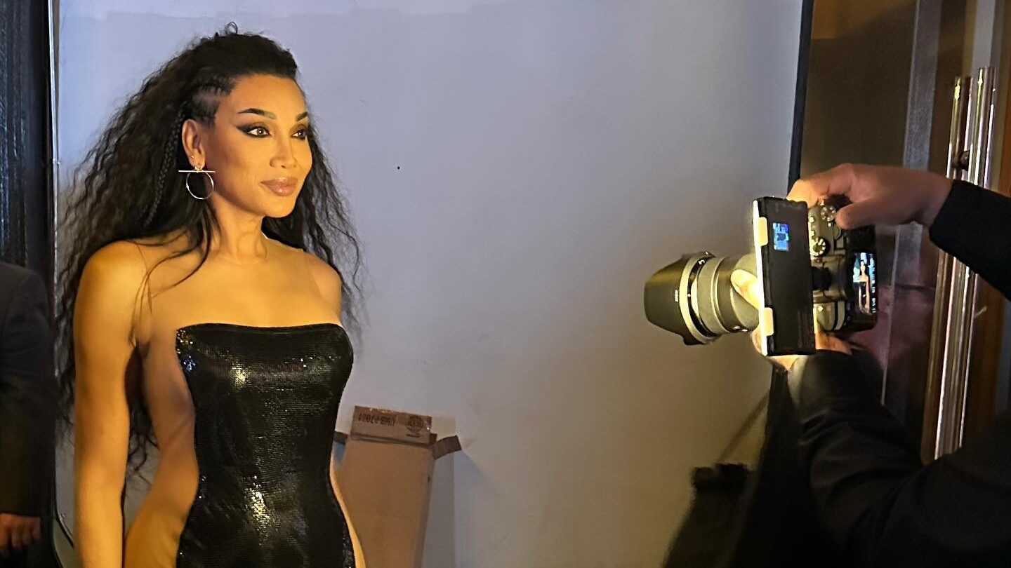 Yasmin Lee dans une robe noire ajustée, posant avec assurance devant un photographe.