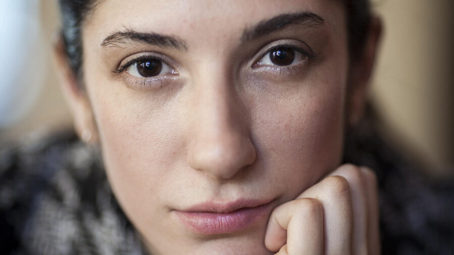 Gros plan d'une jeune femme aux cheveux foncés, appuyant son menton sur sa main, regardant directement l'objectif.