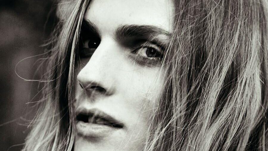 Portrait en noir et blanc du mannequin Andreja Pejić, regardant l’objectif avec un éclairage doux et un arrière-plan naturel.