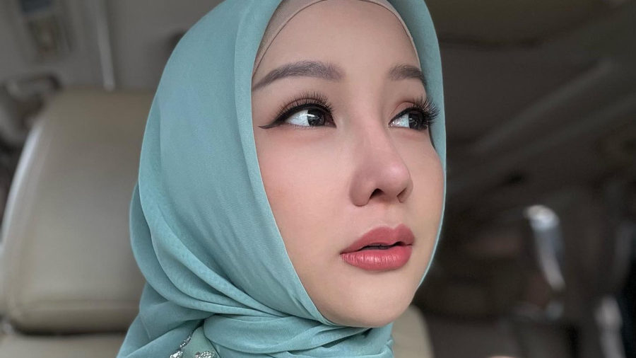 Lucinta Luna porte un hijab vert clair et une robe finement perlée, assise dans une voiture, le regard tourné vers l’extérieur avec une expression douce et posée.