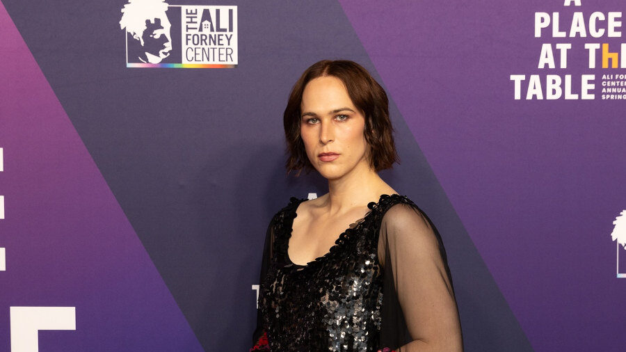 Tommy Dorfman debout lors du gala A Place at the Table, portant une longue robe noire à manches fleuries.