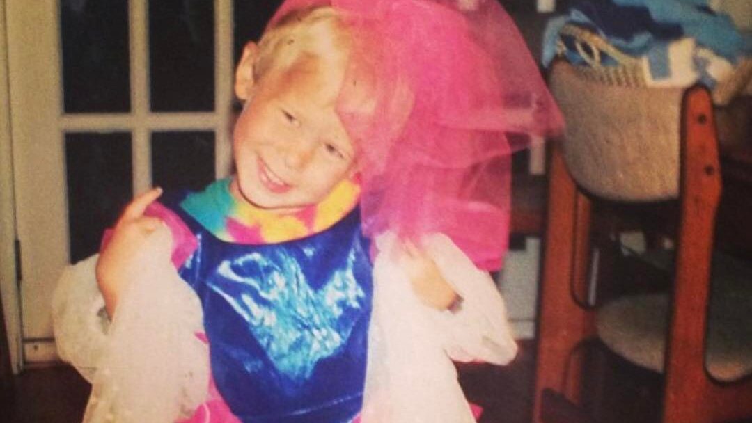 Tommy Dorfman enfant, portant des vêtements colorés de déguisement, souriant avec la tête inclinée dans une pose espiègle.