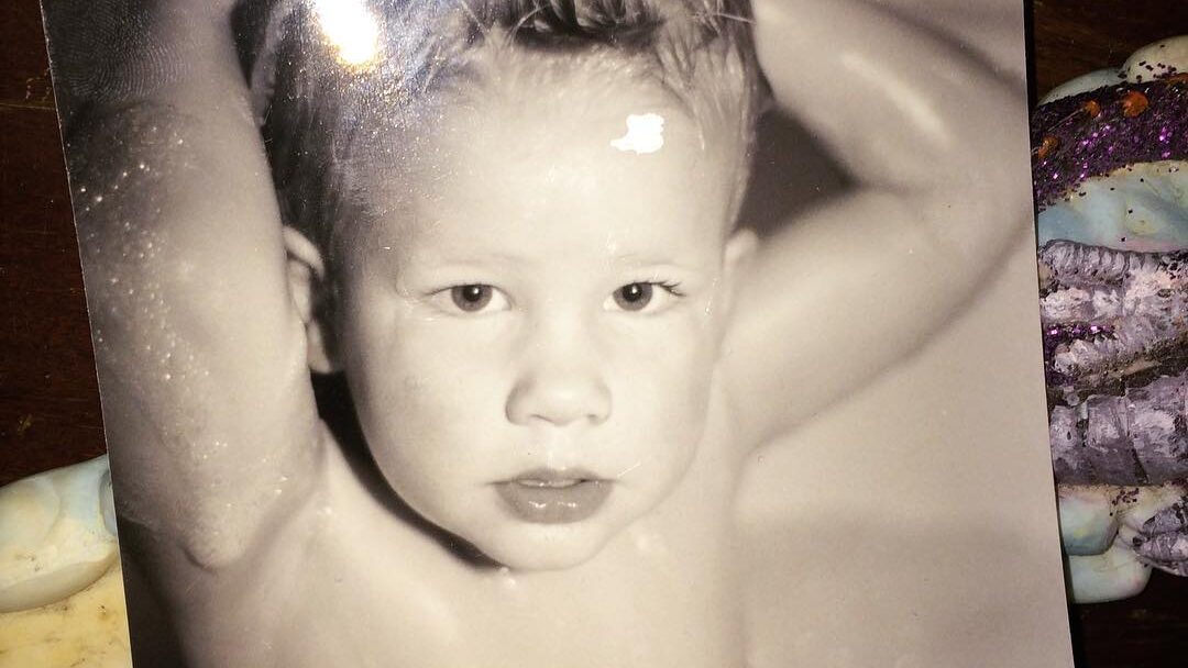 Photo en noir et blanc Willow Pill bébé avec les cheveux mouillés et hérissés, bras derrière la tête.