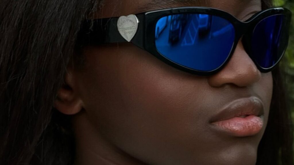 Zaya Wade en portrait rapproché en extérieur, portant des lunettes de soleil modernes et une tenue claire sans manches.