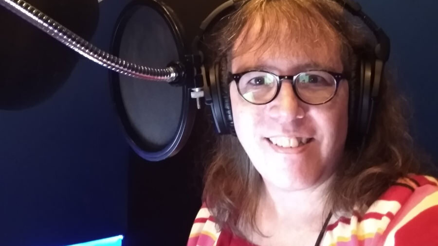Julia Serano dans un studio d’enregistrement avec un casque, souriante près d’un micro après avoir terminé son livre audio.
