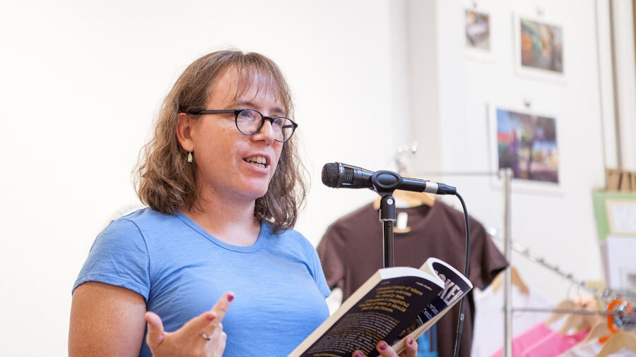 Julia Serano lisant un extrait de son livre Outspoken à un pupitre en 2017, parlant dans un micro tout en tenant un exemplaire.