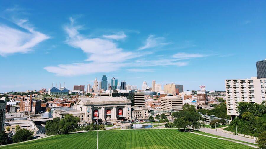 Vue panoramique de la skyline de Kansas City avec Union Station au premier plan et une grande pelouse verte sous un ciel bleu.