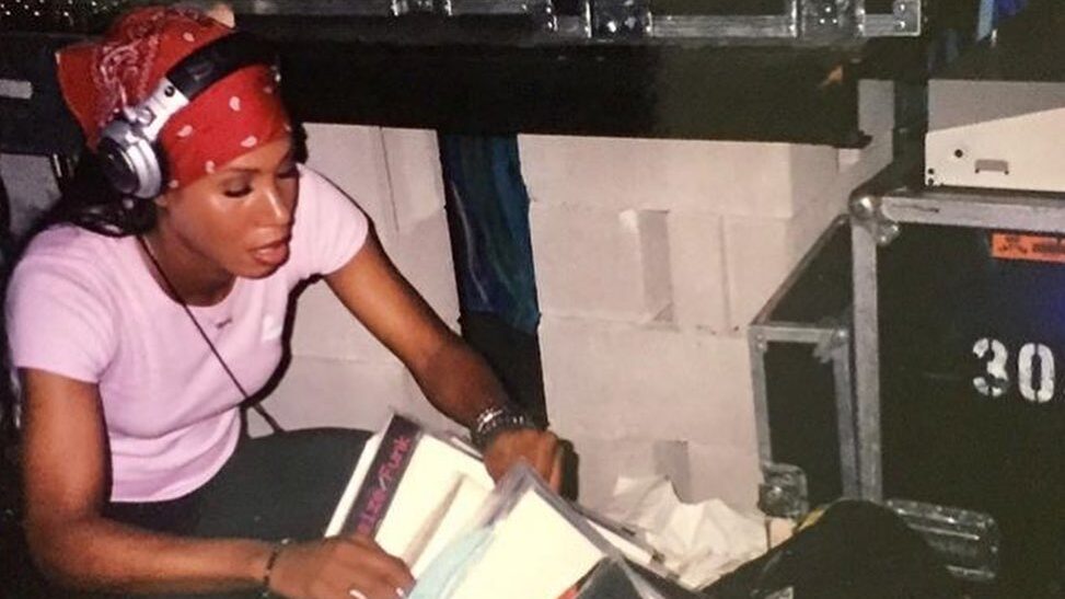 La jeune Honey Dijon assise à côté d’un équipement de DJ à New York, classant des vinyles tout en portant un casque et un bandana rouge.